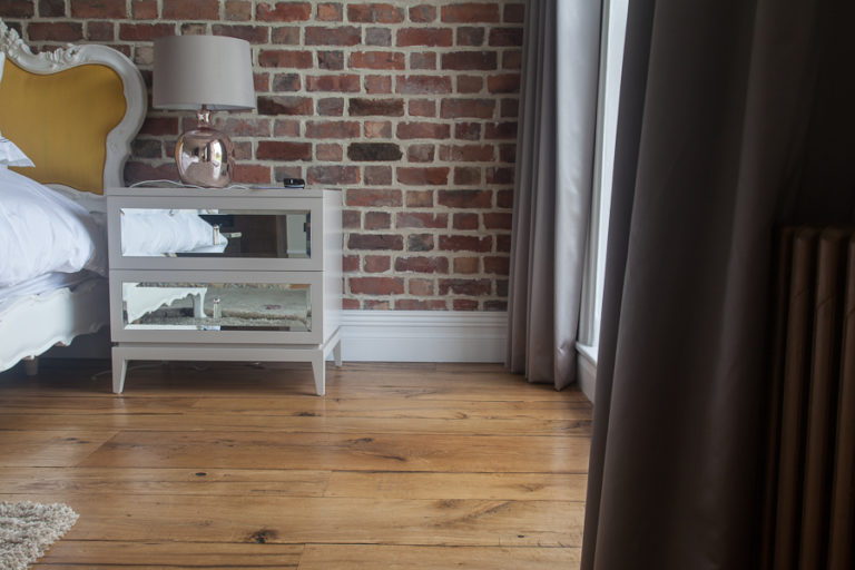 low angle view of bedroom showing antique oak flooring with bedside cabinet and bare brick wall