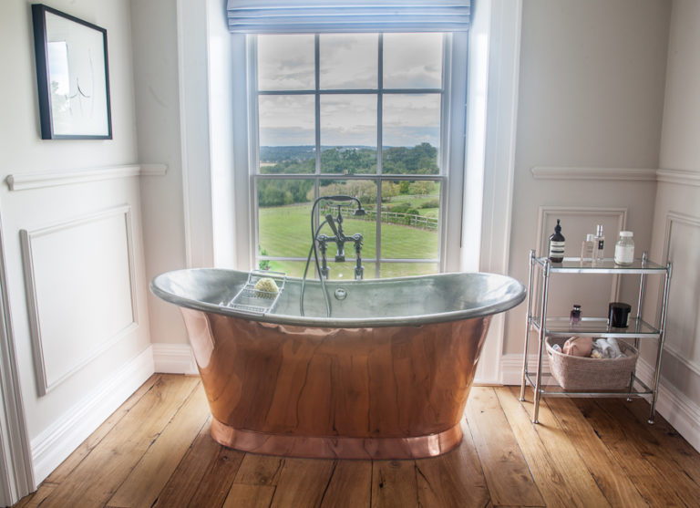 Wide angle view of bathroom with copper bath and window looking out onto fields