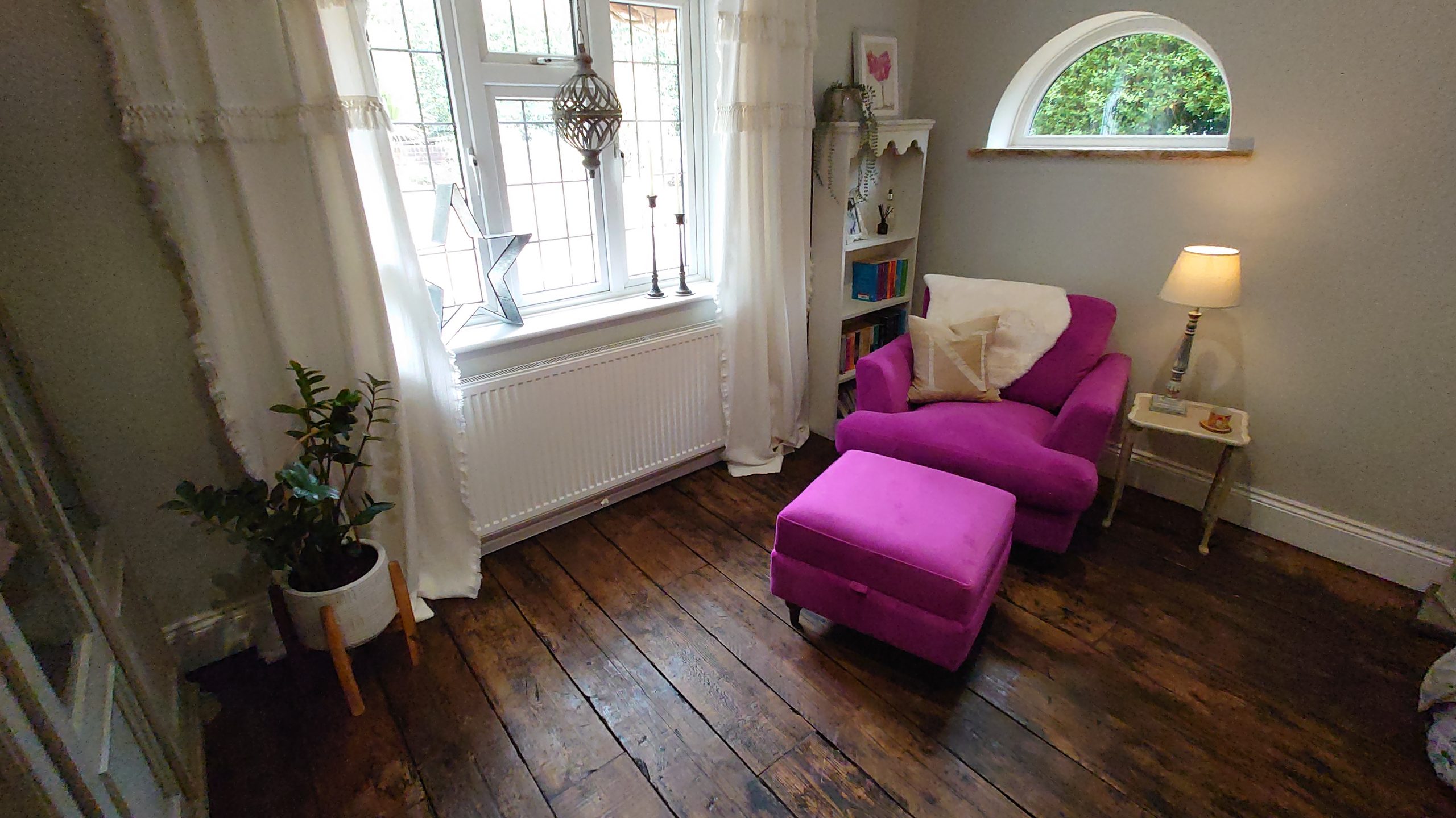 Reclaimed pine scaffold board flooring stained and treated to give the appearance of antique oak, in situ in a living room with a bright purple armchair and footstool in the corner